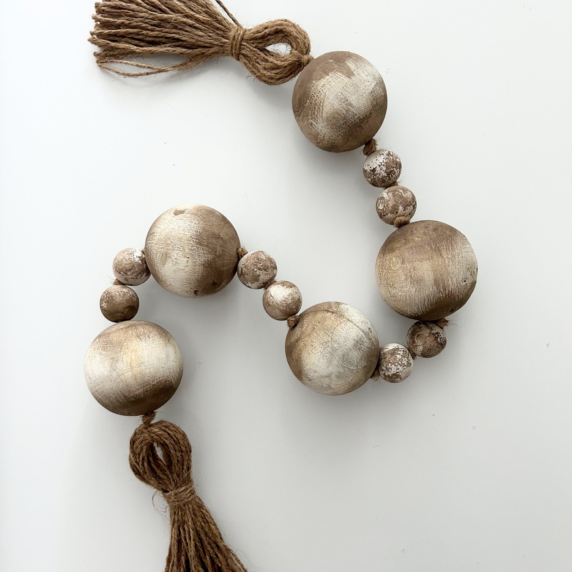 Handmade wooden bead garland with jute tassel styled on white background