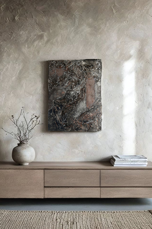 Handmade abstract wall art with black, copper, and earthy textures, displayed on a rustic Japandi-style wall in a modern neutral-toned interior. The artwork is mounted above a wooden console with minimal natural decor, showcasing its raw surface and sculptural relief details.